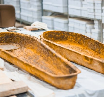 Two rusted metal trays resting on a table covered with fabric and boxes in the background