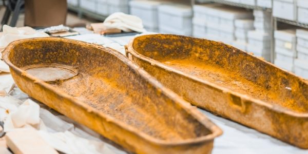 Two rusted metal trays resting on a table covered with fabric and boxes in the background