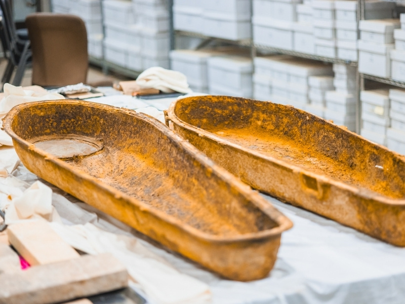 Two rusted metal trays resting on a table covered with fabric and boxes in the background